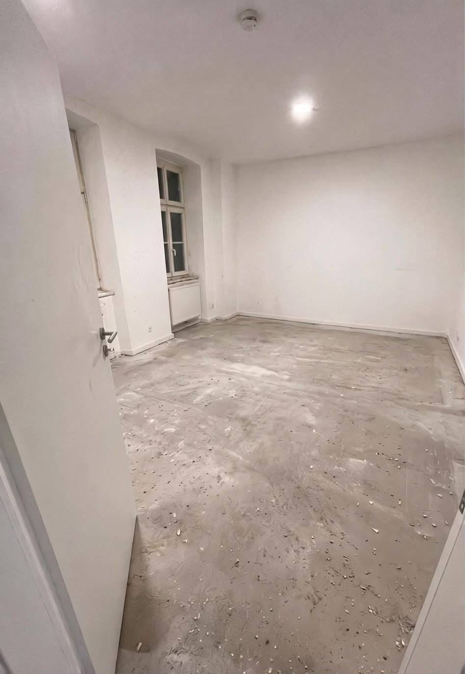 Leerer Altbauraum mit rohem, verschmutztem Estrich vor der Bodenverlegung